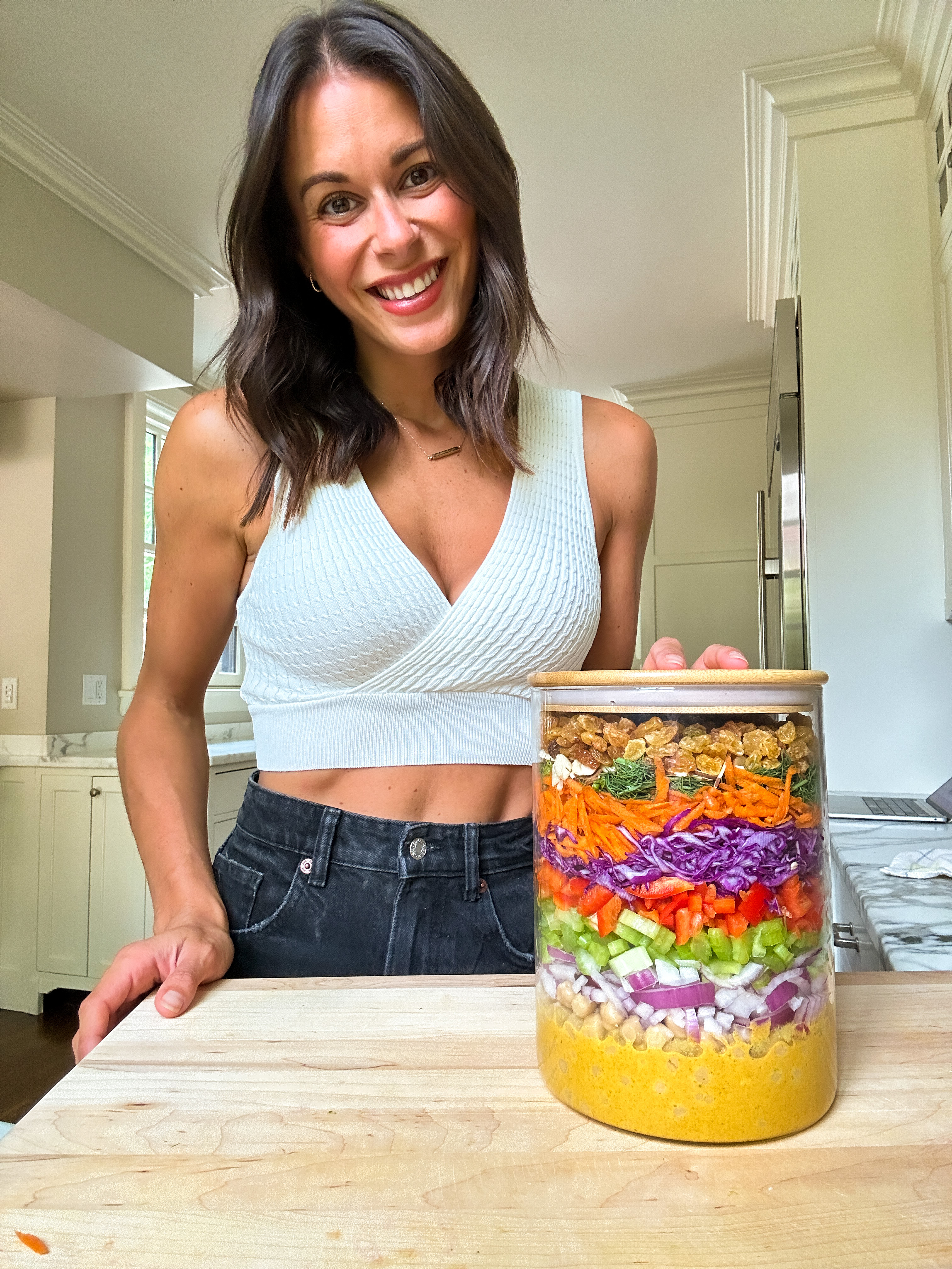 jackie akerberg of jackfruitful kitchen in a kitchen with a clear canister filled with colorful beautiful layers of salad ingredients for her viral layered curry chickpea salad